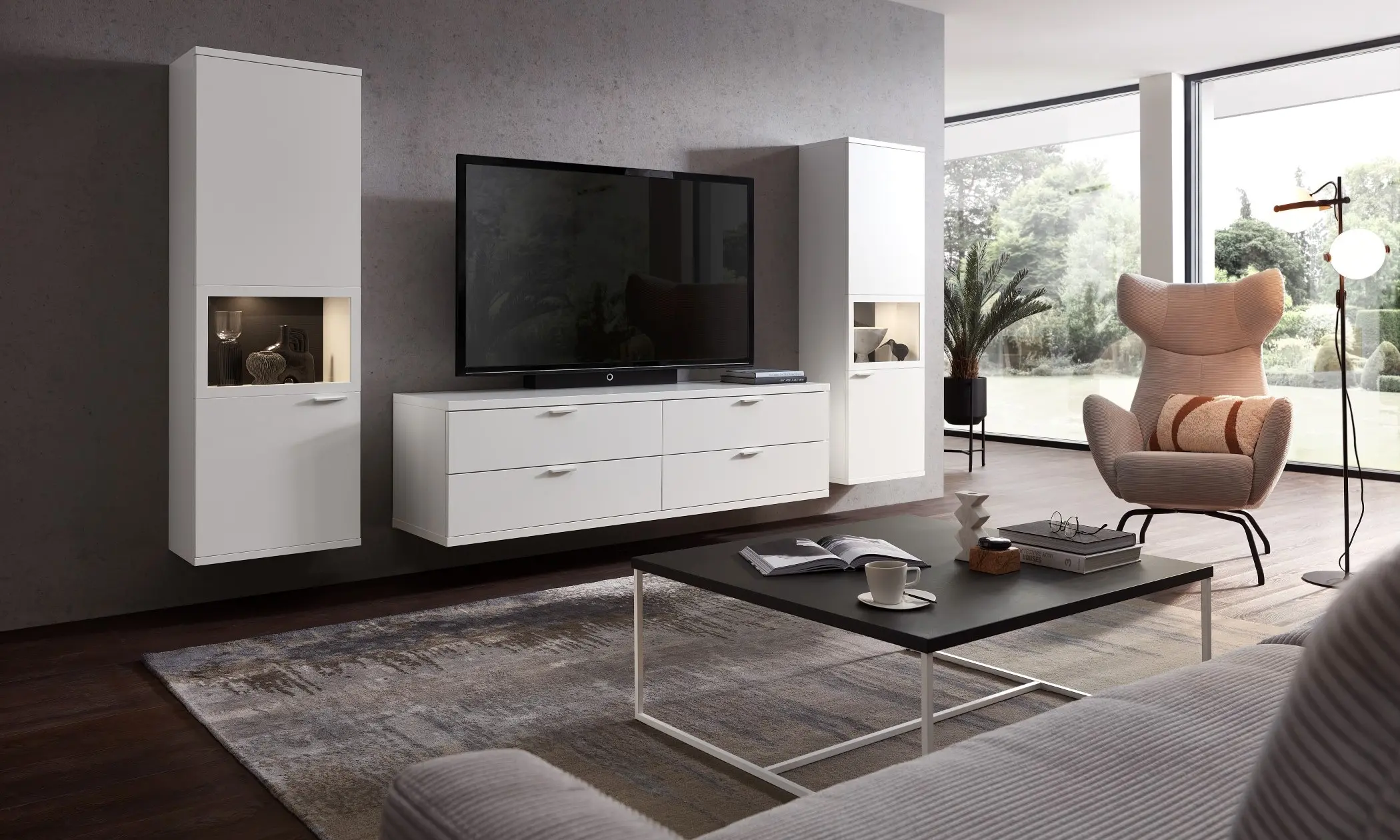 Auf dem Bild sieht man ein weißes Lowboard und 2 hängende Highboards die beleuchtete Vitrinen beinhalten.